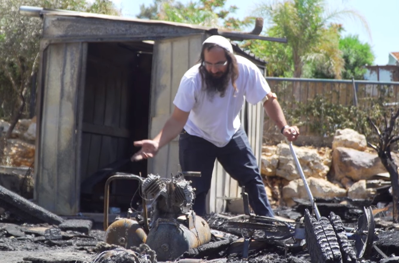 דוד גוטמן על רקע ביתו שנשרף